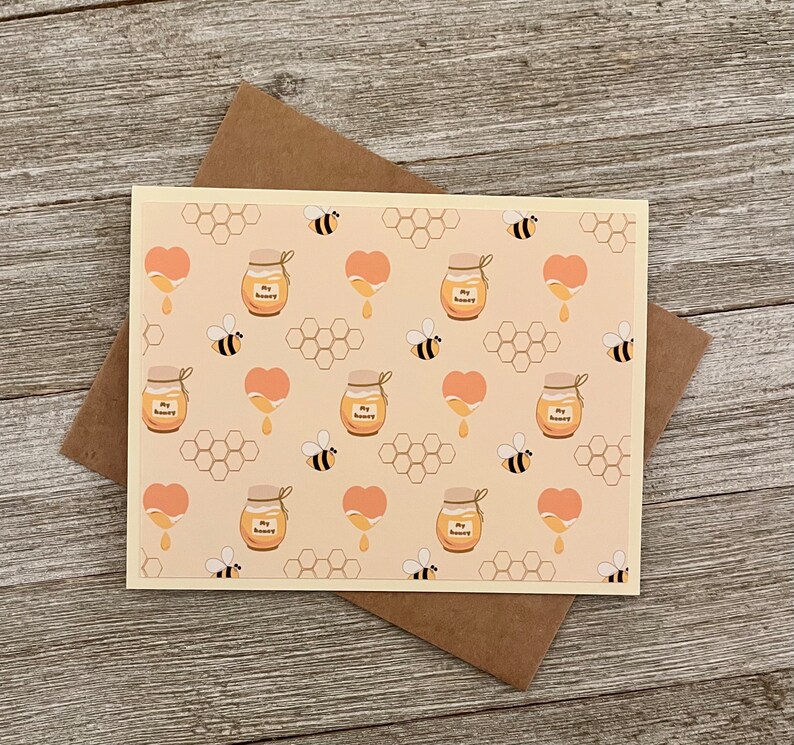 Puede incluir: Una tarjeta de color amarillo claro con un patr&oacute;n repetido de tarros de miel, panales, corazones y abejas. Los tarros de miel est&aacute;n etiquetados con "My Honey".