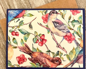 May include: A greeting card with a watercolor design featuring three birds perched on branches with red berries. The birds are a blue bird, a gray bird, and a brown bird. The background is a cream color with green leaves.