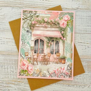 May include: A pink and white building with a pink awning and a floral design. There are tables and chairs outside the building, and there are flowers and greenery around the building.
