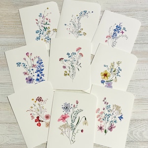 May include: Set of ten blank greeting cards featuring watercolor illustrations of various wildflowers in shades of blue, pink, and yellow. The cards are perfect for sending a heartfelt message to a loved one.