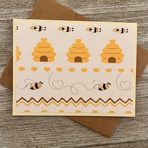 Puede incluir: Una tarjeta beige con un patr&oacute;n de colmena y abejas. La tarjeta tiene un sobre marr&oacute;n.