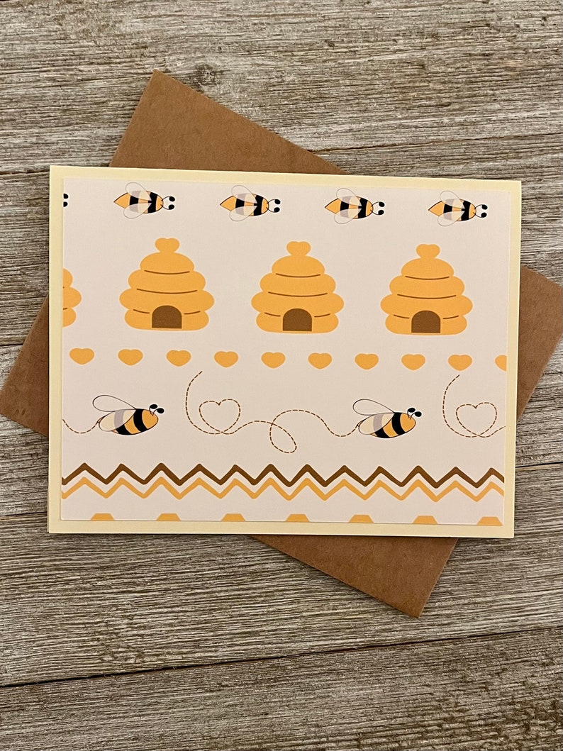 Puede incluir: Una tarjeta beige con un patr&oacute;n de colmena y abejas. La tarjeta tiene un sobre marr&oacute;n.