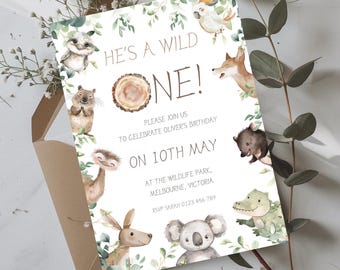Puede incluir: Una tarjeta de invitación blanca con una ilustración de acuarela de varios animales australianos, incluyendo un koala, un canguro, un wombat y un cocodrilo. El texto dice "He's a Wild One!" e incluye detalles para una fiesta de cumpleaños.