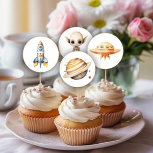 May include: Set of six cupcake toppers featuring space-themed illustrations. The toppers include a rocket, a UFO, an alien, Saturn, and stars. The toppers are printed on white cardstock and are perfect for adding a fun touch to your space-themed party.