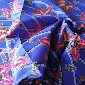 Può includere: Tessuto blu con un motivo ripetuto di fiori rosa, gialli e verdi. Il tessuto ha un motivo a righe bianche e nere sui bordi. Il testo "VERITABLE JAVA" è stampato sul tessuto.