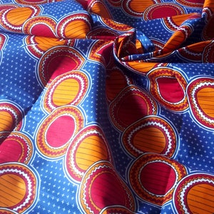 以下が含まれることがあります： オレンジ、赤、白の円が繰り返される模様の青い布。布は折り畳まれており、表面は質感がある。