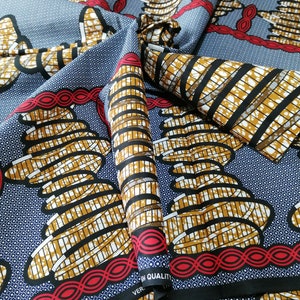 May include: A close-up of a blue and gold patterned fabric with a red and white border. The fabric has a repeating pattern of stacked circles with a black and white grid design. The fabric is folded in half, and the text "VER- HIGH QUALITY" is visible on the bottom right corner.