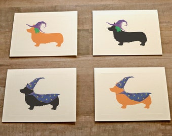 May include: Four rectangular greeting cards featuring silhouettes of corgi dogs. Two cards show orange corgis wearing purple witch hats with green hair, and two cards show black or orange corgis wearing blue wizard hats and capes with yellow stars.
