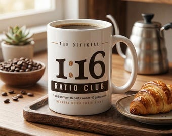 May include: A white ceramic coffee mug featuring the black text THE OFFICIAL 1:16 RATIO CLUB with coffee bean icons replacing the colon. Below the text, it reads 1 part coffee 16 parts water 0 guesswork and MEMBERS WEIGH THEIR BEANS.