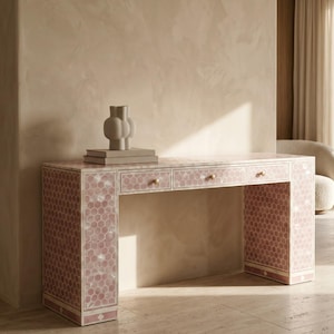 May include: A rectangular console table featuring a pink and white hexagonal tile pattern across its surface. The table includes three drawers, each equipped with a small, round, gold-toned knob. A light-colored, abstract-shaped vase sits on top.