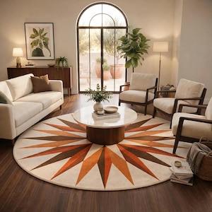 May include: A large circular area rug featuring a prominent sunburst pattern in shades of burnt orange and dark brown against a cream-colored background, centered beneath a round white marble coffee table with a dark wood cylindrical base.