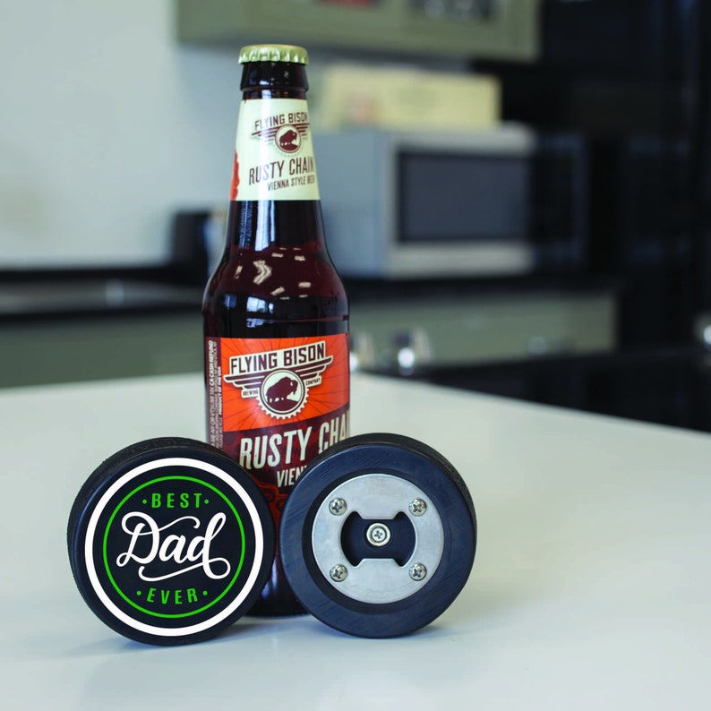 Peut inclure: Deux ouvre-bouteilles en forme de rondelle de hockey noires. L'un a un ouvre-bouteille en m&eacute;tal et l'autre porte le texte "Best Dad Ever" en lettres vertes et blanches.