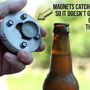May include: A baseball-shaped bottle opener with magnets to catch the cap. The opener is made of metal and has a red and white baseball stitching design. The cap is being held by the magnets.