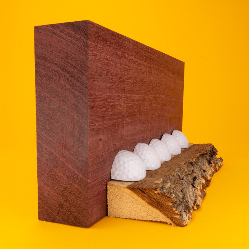 May include: A wooden board with a dark reddish-brown finish stands upright against a yellow background. A row of white golf balls are arranged on a piece of bark attached to the bottom of the board.