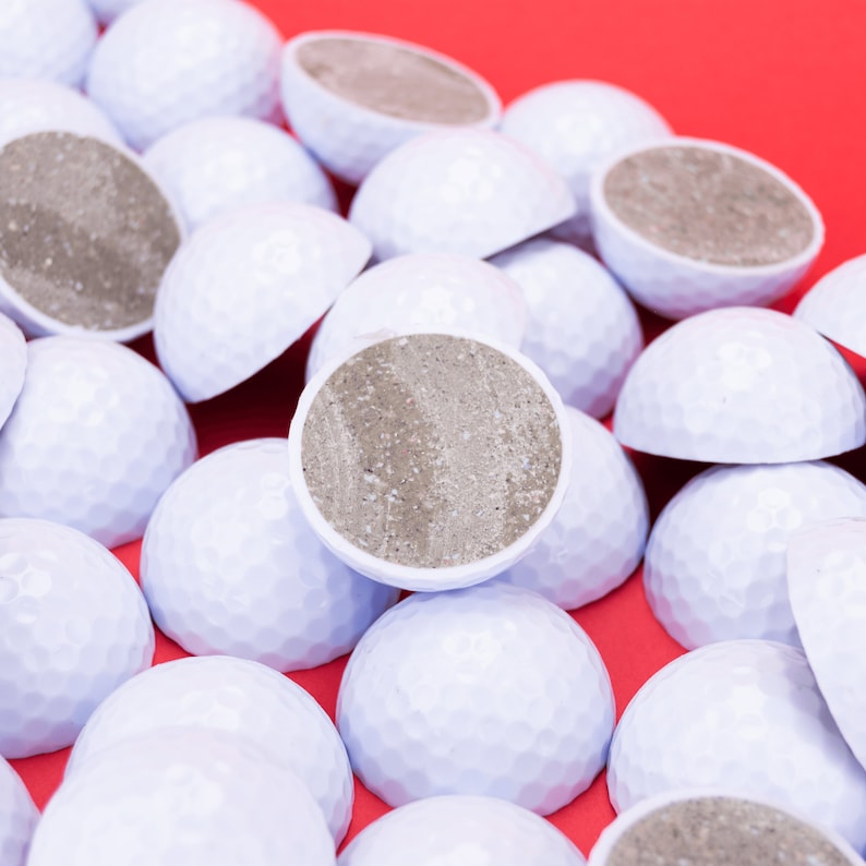 May include: A close-up of a pile of white golf balls with a gray, textured surface on a red background.