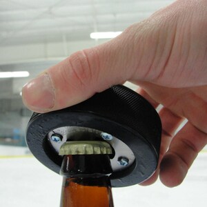 Peut inclure: Un ouvre-bouteille en forme de rondelle de hockey noir utilis&eacute; pour ouvrir une bouteille de bi&egrave;re en verre brun.