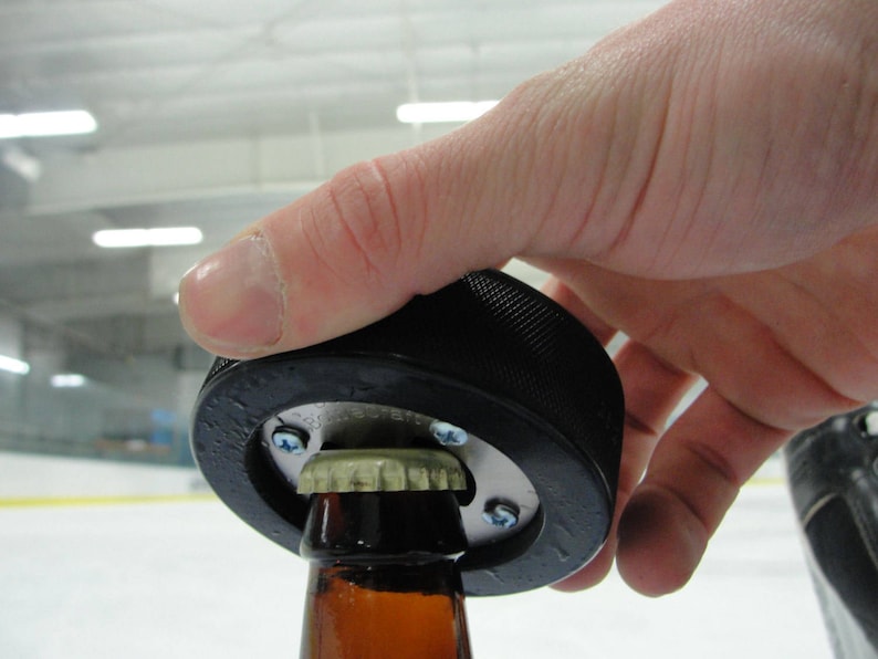 Peut inclure: Un ouvre-bouteille en forme de rondelle de hockey noir utilis&eacute; pour ouvrir une bouteille de bi&egrave;re en verre brun.