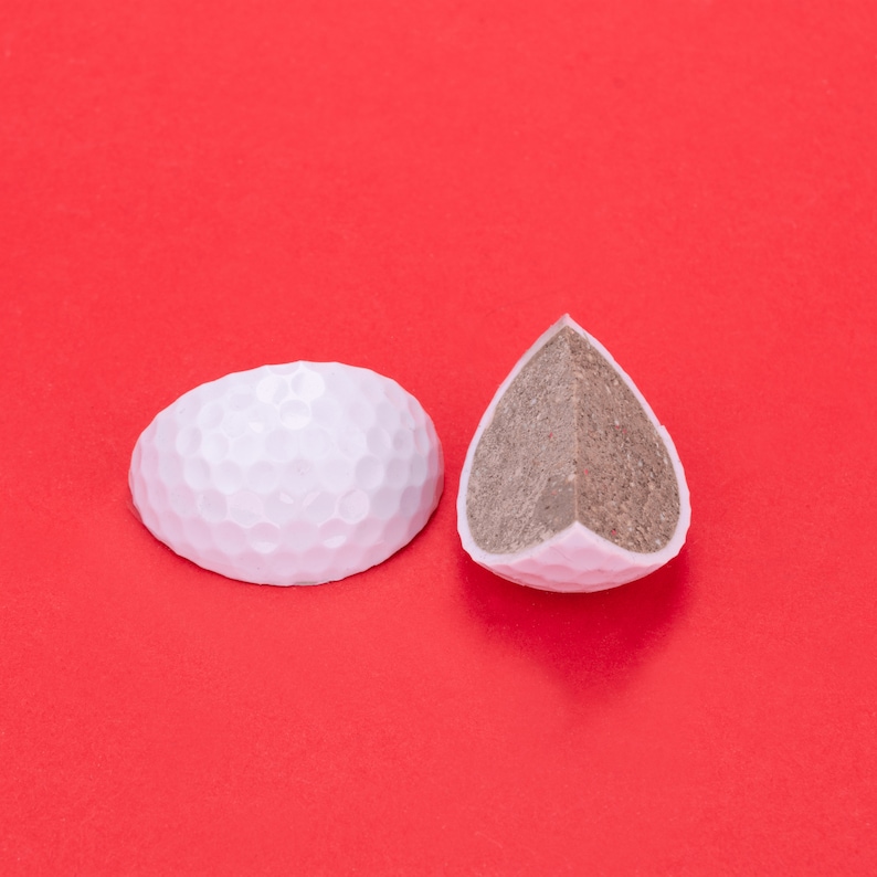 May include: Two white chocolate golf ball candies, one whole and one cut in half to reveal a brown chocolate filling.