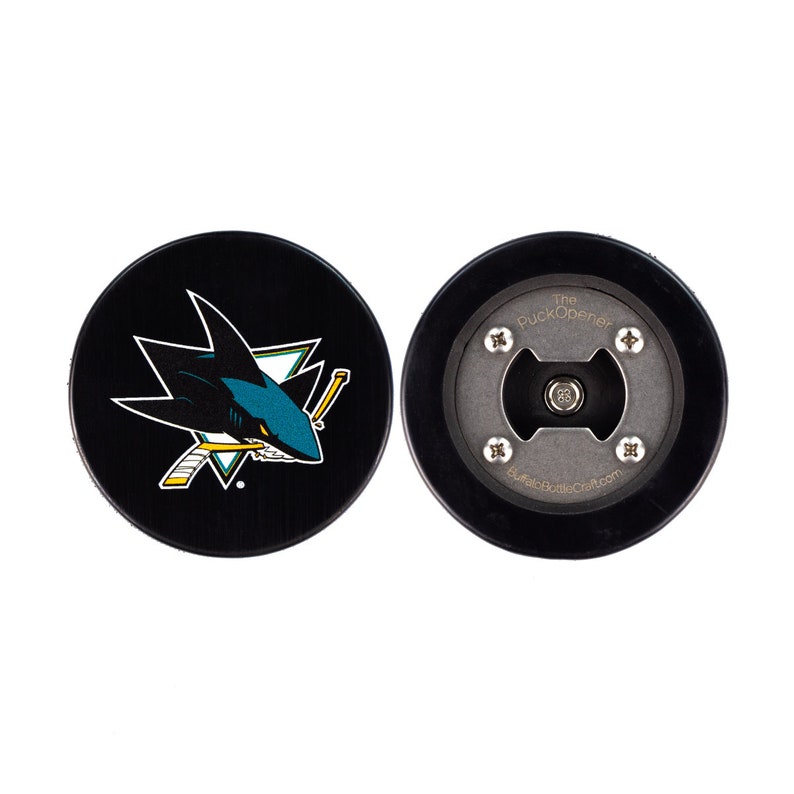 以下が含まれることがあります： 片側にサンノゼ・シャークスのロゴ、もう片側に「The Puck Opener」の文字と栓抜きがついた、黒と白のホッケーパック栓抜きです。