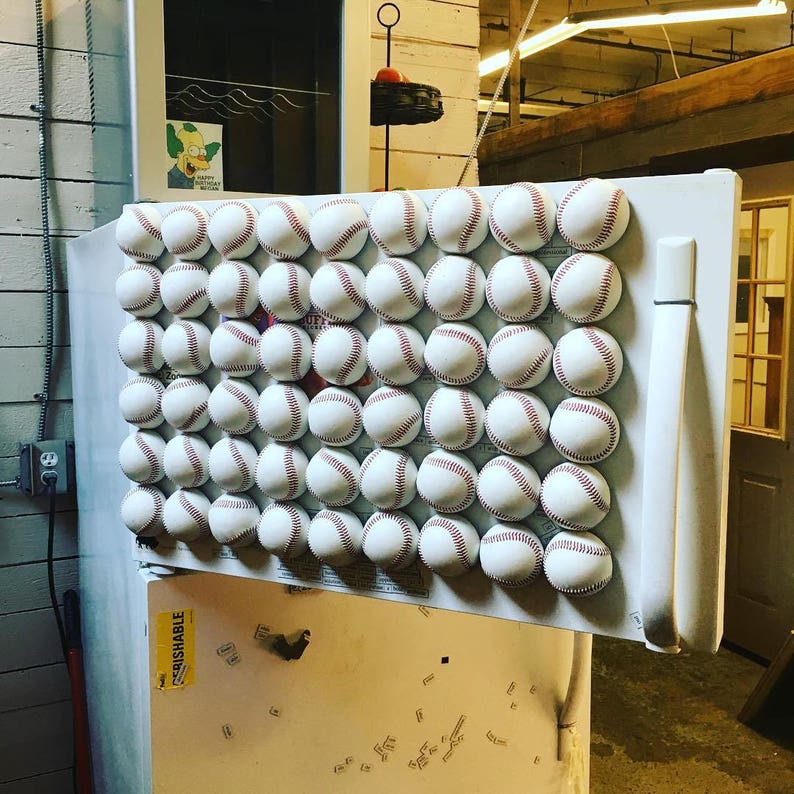 May include: A white refrigerator door with a grid of 42 white baseballs attached with magnets. The baseballs are arranged in 7 rows of 6 baseballs each.