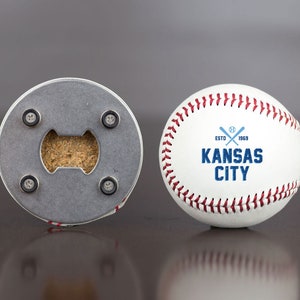 Pu&ograve; includere: Una palla da baseball bianca con cuciture rosse e un logo blu che dice "ESTD 1969 KANSAS CITY" con mazze da baseball incrociate. Il retro della palla da baseball &egrave; un apribottiglie con un tappo.
