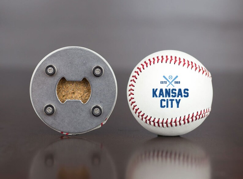 Pu&ograve; includere: Una palla da baseball bianca con cuciture rosse e un logo blu che dice "ESTD 1969 KANSAS CITY" con mazze da baseball incrociate. Il retro della palla da baseball &egrave; un apribottiglie con un tappo.