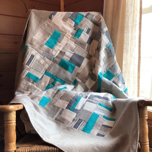 May include: A patchwork quilt with a geometric design in shades of grey and teal, draped over a wooden rocking chair.