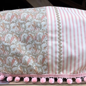 Può includere: Una copertura per macchina da cucire con motivo floreale rosa e marrone con una sezione a righe rosa e bianche. La copertura ha un bordo di pon pon rosa.