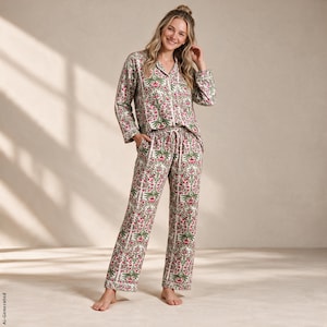 May include: A two-piece pajama set featuring a long-sleeved button-down shirt and matching straight-leg pants. The fabric is off-white with a repeating vertical pattern of pink flowers and green leaves, finished with white piping trim.