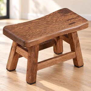 May include: A small, low-profile wooden stool featuring a rectangular seat with rounded edges and a visible wood grain pattern. The stool is supported by four sturdy, slightly angled legs connected by horizontal support bars on all sides.