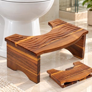 May include: A brown wooden toilet stool with a curved cutout design and wavy grooved patterns on the top surface. The stool features a sturdy base with arched sides, and a second, identical smaller stool is positioned flat on the floor nearby.