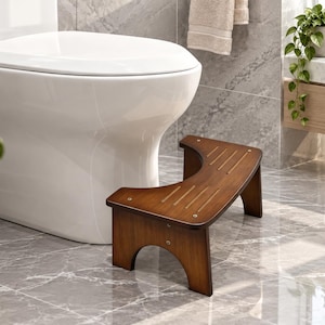 May include: A dark brown wooden bathroom stool with a curved, crescent-shaped design that fits around the base of a toilet. The stool features a flat top surface with three parallel grooved lines for grip and is supported by two arched side legs.
