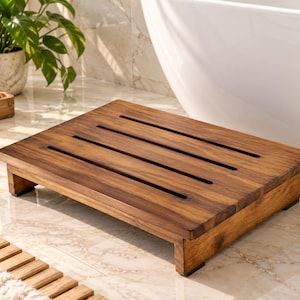 May include: A rectangular wooden shower platform featuring a rich brown grain and four parallel horizontal slats. The low-profile design is supported by sturdy wooden legs with small black non-slip pads at each corner, providing a stable base.