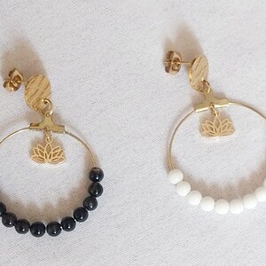 Peut inclure: Une paire de boucles d'oreilles créoles dorées avec un clou circulaire texturé, une breloque fleur de lotus suspendue et une rangée partielle de perles. Une boucle a des perles noires, l'autre des perles blanches, avec fermoirs à tige.