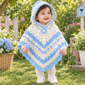 May include: A crochet hooded poncho featuring a V-shaped pattern in alternating cream and light blue yarn. The garment includes a scalloped edge along the bottom hem and a single decorative circular button closure at the neckline in cream and blue.