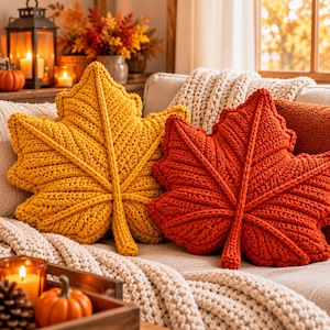 May include: Two decorative throw pillows shaped like maple leaves, one in a vibrant mustard yellow and the other in a deep burnt orange. Both pillows feature a chunky knit texture with raised, braided-style veins radiating from the center stem.