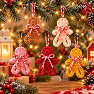 May include: Five crocheted gingerbread-style ornaments in brown, cream, pink, red, and yellow. Each figure features a red and white striped string loop for hanging and a matching red and white striped bow tied around the neck area.