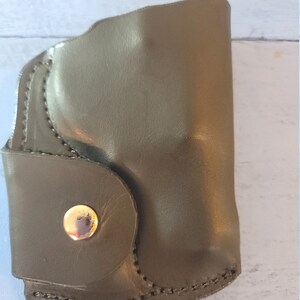 May include: A dark green leather holster with a gold snap closure.
