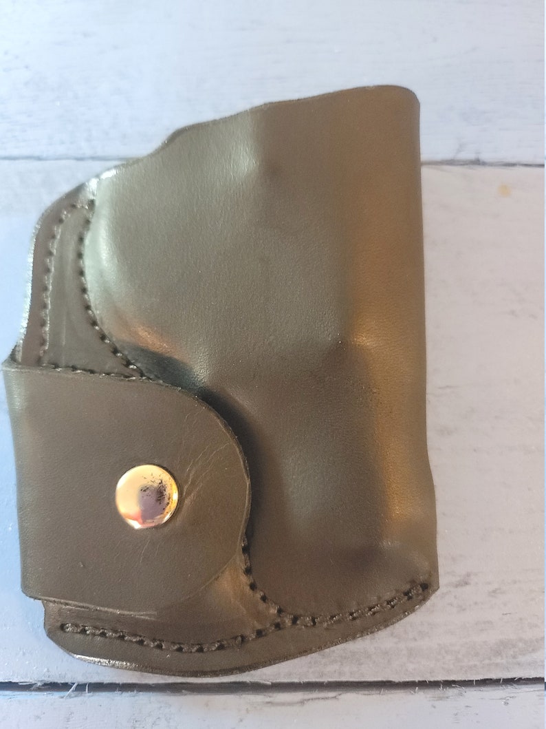 May include: A dark green leather holster with a gold snap closure.
