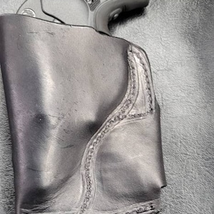 May include: A black leather holster with a stitched design, holding a black handgun with a silver barrel and a black grip. The gun has a silver inscription that reads "380".