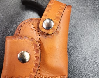 May include: A brown leather holster with a decorative stitching pattern and two silver snaps. A black handgun is inside the holster.