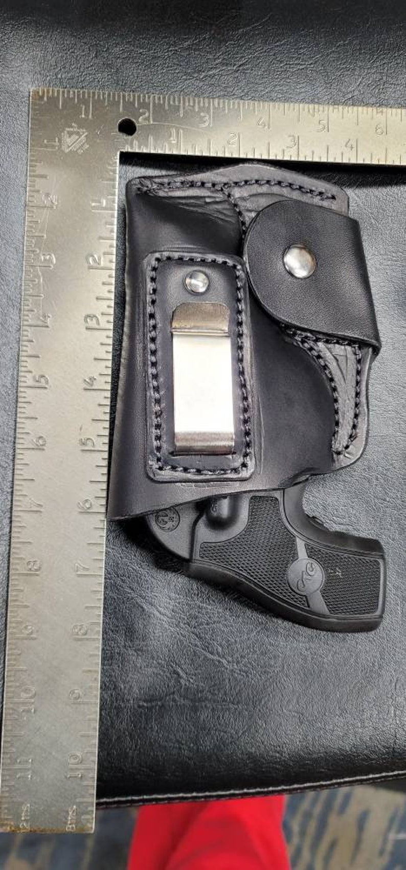May include: A black leather holster with a metal clip and a black handgun inside. The holster has a flap with a snap closure.