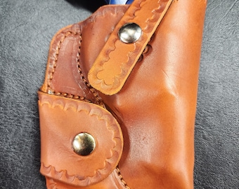 Op de afbeelding: Een bruine leren holster met een blauw pistool erin. De holster heeft decoratieve stiksels en een drukknopsluiting.