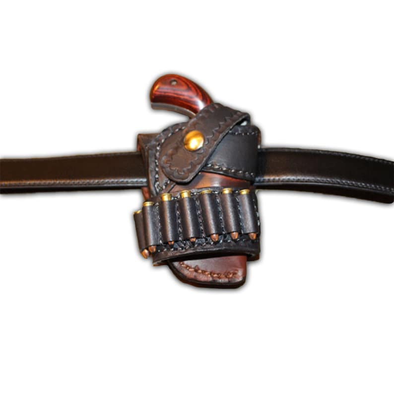 K&ouml;nnte beinhalten: Ein schwarzes Lederholster mit einer braunen Pistole mit Holzgriff und einem schwarzen Leder-Munitionshalter mit Patronen. Das Holster ist an einem schwarzen Lederg&uuml;rtel befestigt.