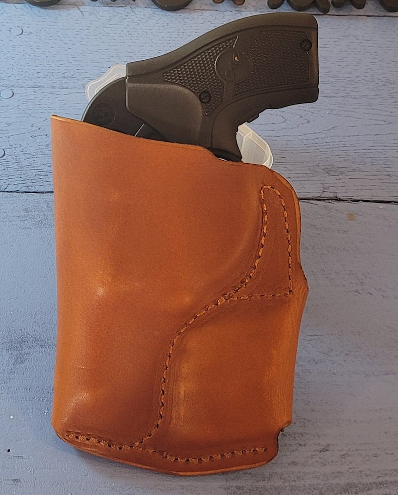 May include: A brown leather holster for a small handgun. The holster has a stitched design and is made of a high-quality material.