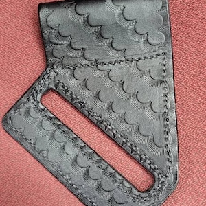 May include: A black leather wallet with a unique embossed pattern. The wallet has a single slot for holding cards or cash.