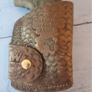 May include: A brown leather holster with a gun inside. The holster has a decorative pattern and the text "The Right to Keep and Bear Arms".