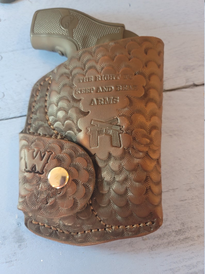 May include: A brown leather holster with a gun inside. The holster has a decorative pattern and the text "The Right to Keep and Bear Arms".