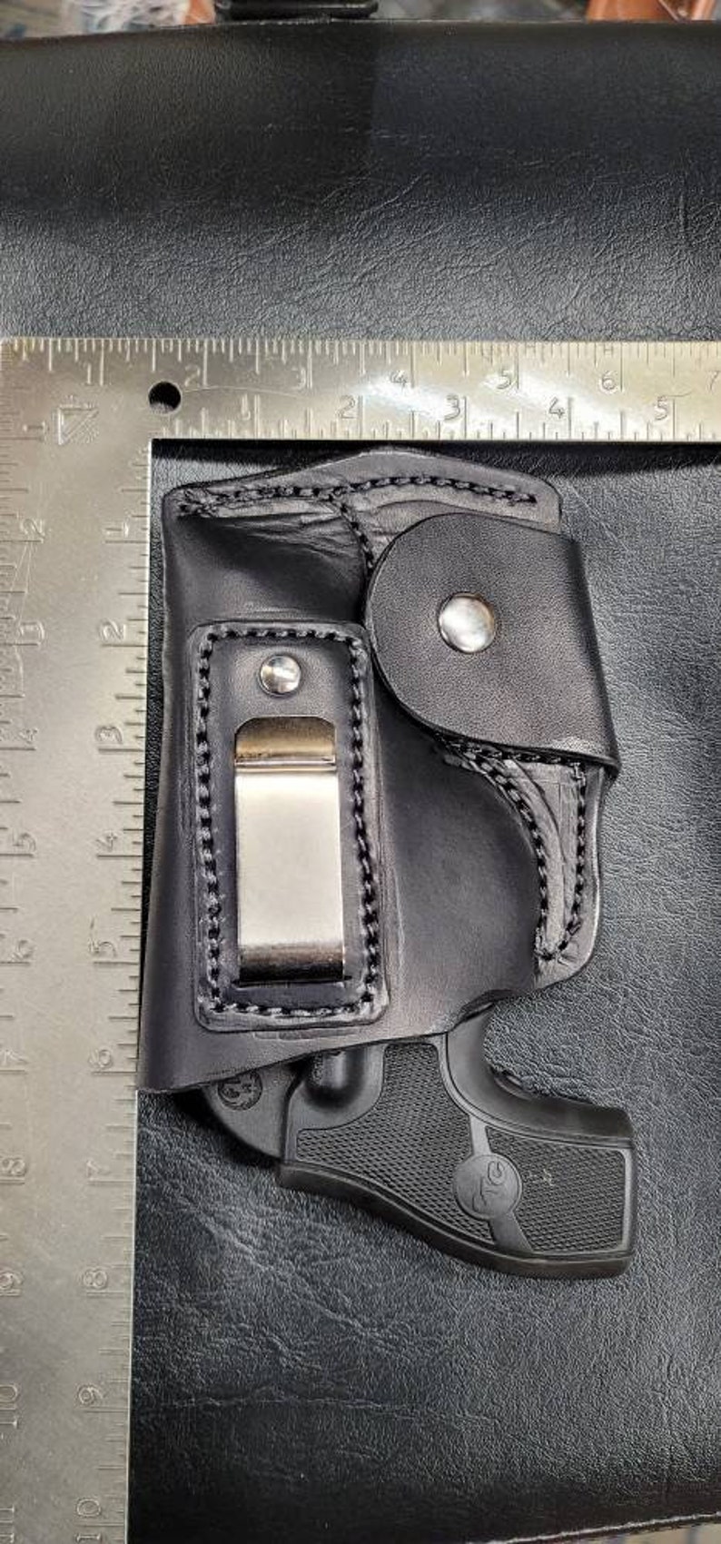 May include: Black leather holster with a clip and a black handgun inside. The holster has a flap with a snap closure.