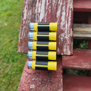 May include: Six yellow and silver shotgun shells with black rubber bands holding them together.